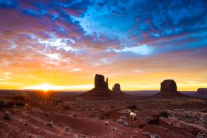 Wild horse crossing the stunning breadth of Monument Valley at sunrise.